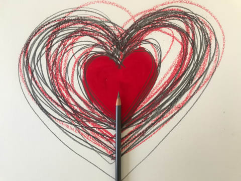 Hand-drawn red heart surrounded by many other heart outlines drawn in black and red pencils