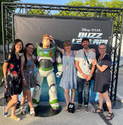 A photograph of people posing in front of a human-sized Buzz Lightyear figurine.