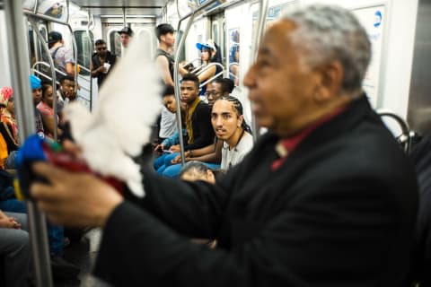 Color photo on a NYC subway with an out of focus man performing magic with a dove flying in front of his face. The background is in focus showing the faces of the onlookers.