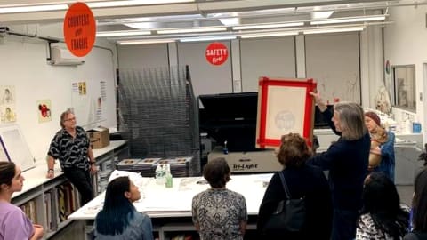 A group of people in the SVA printshop talking in a circle. Someone is showing the group a prepared screen printing screen. 