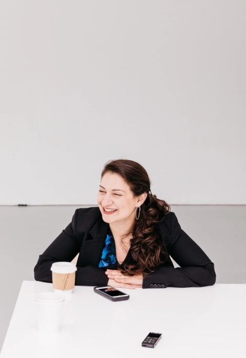 a woman in a blazer sits at a table with her arms folded