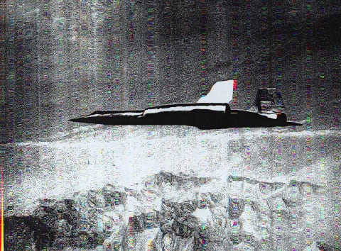 Grainy black & white photograph showing a supersonic jet in profile view flying above mountains, distorted by scanner manipulation. 