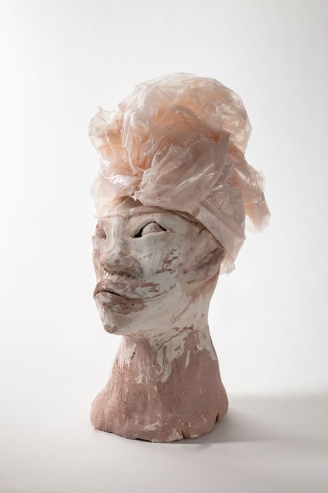 A sculpture by Symia McKellar. The sculpture is a human head with neck. The sculpture has a surface of marbled pink and white with a textile wrapped head piece.