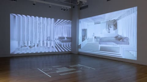 Photograph of gallery corner, showing two oversized projections of a designed interior space with many vertical lines and horizontal shadows throughout the bedroom. On the floor, in the center of the space, is a projection of the floor plan.