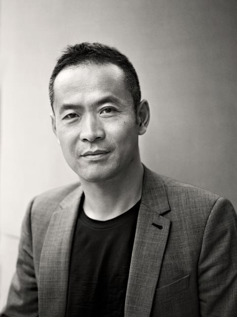 A black and white photograph of curator, ZHANG Ga. Zhang is an asian male wearing a black t-shirt and a suit jacket.