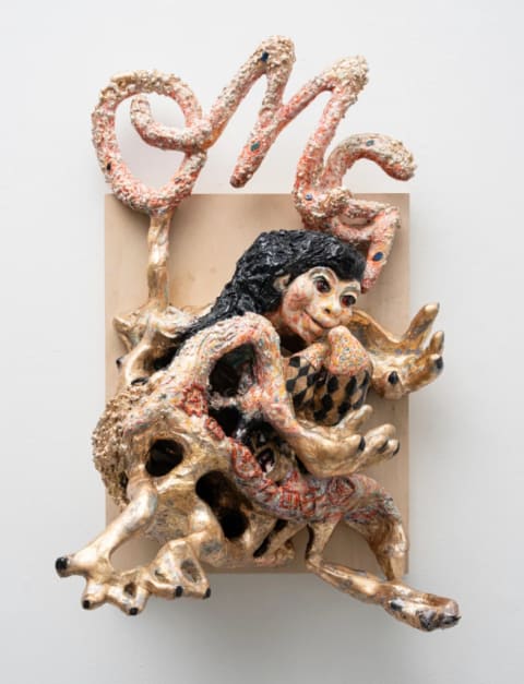 A sculpture of a figure abstracting into various swirling parts and appendages mounted on a wood board