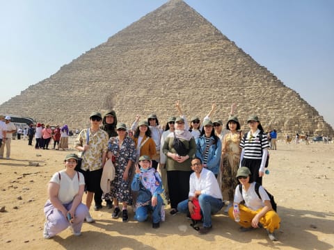 A group photo of 15 people, including teachers and students. They are standing in front of a pyramid. It is sunny and bright out.