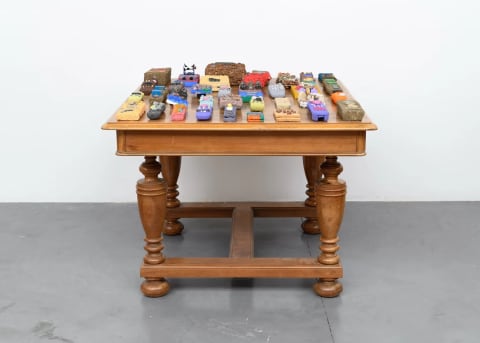 A square wooden table in a white room with many little colorful sculptures on top of it