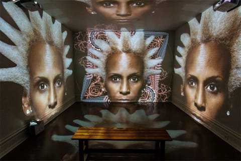 A room with all walls, ceiling and floor covered with projection images of a woman's face.