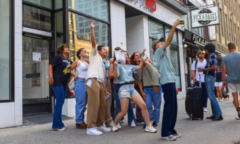 A group of students stand outside on the sidewalk and pose for a selfie