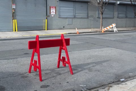 A photograph of an all-red construction barrier standing on an otherwise empty city street during daytime.