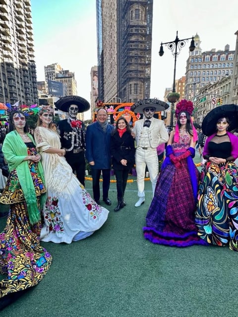 A group photo of 8 people posed in front of the flatiron building at a Día de Muertos celebration—5 are in festive dress