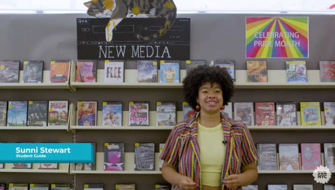 A woman in a striped shirt stands in front of a shelves lined with DVD's in a library