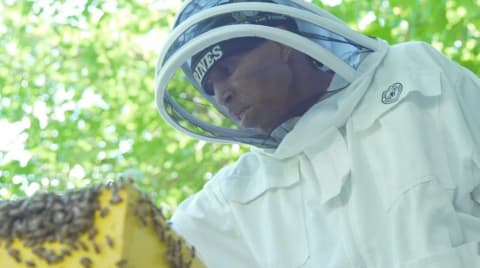 A man in a beekeeper suit with a box of bees in front of him