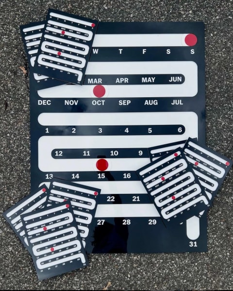 A calendar consisting of a channel that moves past months and numbered days with a movable red dial 