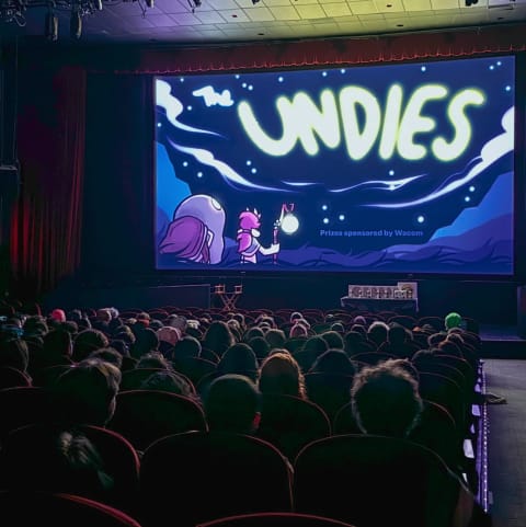 A theatre filled with people and a slide on the screen that reads "The Undies" in a dark blue sky