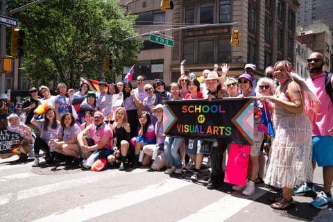 A group photo of students and faculty holding up a flag that reads "School of Visual Arts" in pride colors. They are standing on West 28th street as part of the NYC Pride Parade.