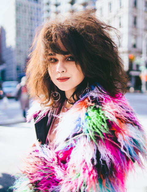 <p "="">A young woman in a multicolored coat on a New York City street.
