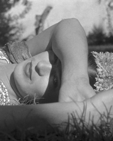a B&W photograph of artist Frida Khalo, lying down, her arm draped across her eyes