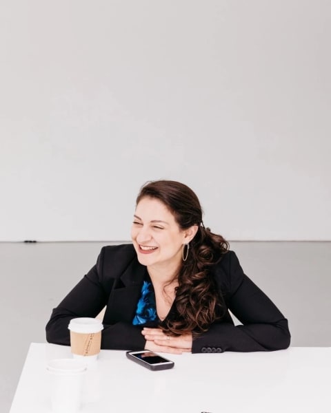 a woman in a blazer sits at a table with her arms folded
