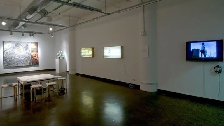 A large white room with a dining table on the floor, a TV on one wall and art work on the others.