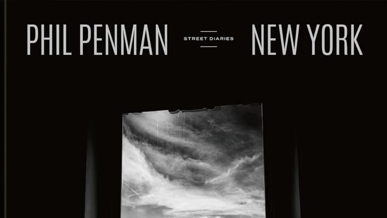 The cover of Phil Penman's book, "New York Street Diaries" which features a black-and-white photograph of the NYC skyline seen outside of a window.
