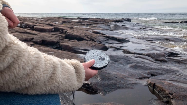 Image of someone holding a stone in front of a rocky beach with water pooling in the rocks