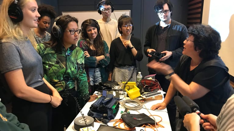 Group of students surrounding table full of equipment in Sound Class with Instructor
