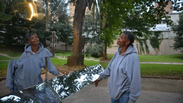 Image of a woman in a grey sweatshirt looking at her reflection in a mirrored sculpture in the park. The Battle Is Joined, Monument Lab, Mural Arts, Public art commission, Vernon Park, Philadelphia, PA, 2017