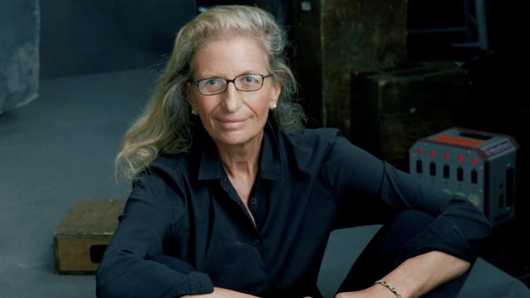 Color photograph on Annie Leibovitz sitting on the floor of a photographic studio looking into the camera. 