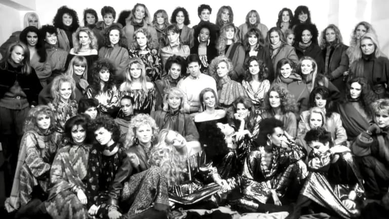 A group of female fashion models posing for a group portrait, with fashion designer Calvin Klein at the center. 