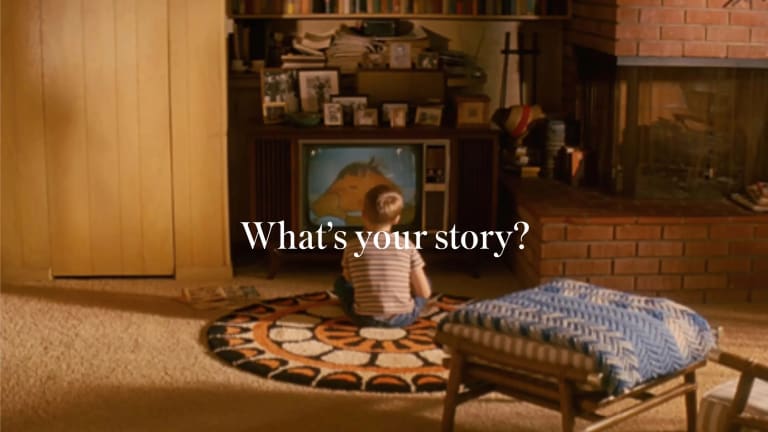 Photo of a boy sitting on the carpet of a living room. He faces a TV. Atop the image are the words, "What's your story?"