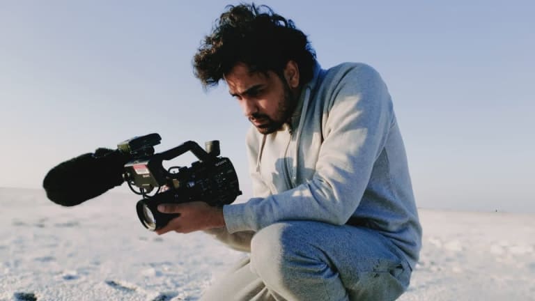 a man in a grey track suit films in India's White Desert, he crouches with a focused look towards his camera