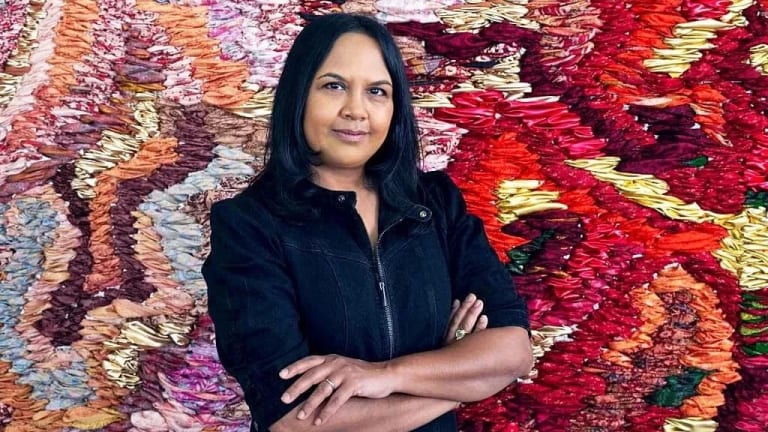 Suchitra Mattai in front of a colorful woven artwork