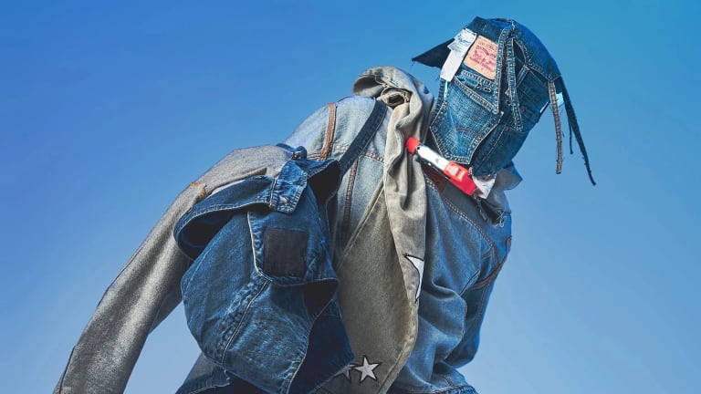 A studio fashion portrait of someone in an all-denim blue outfit and wearing a mask made of denim.