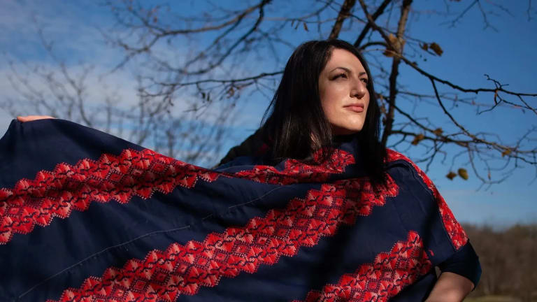 Wafa Ghnaim wearing a piece of Tatreez embroidery with red and blue colors, standing outside