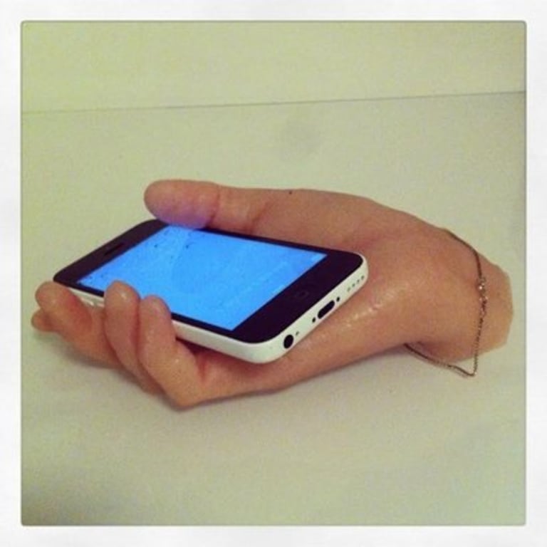 A synthetic hand with a thin bracelet holding a smart phone..