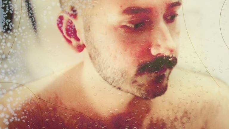 A mustached man, shirtless, seen through a frosted glass.