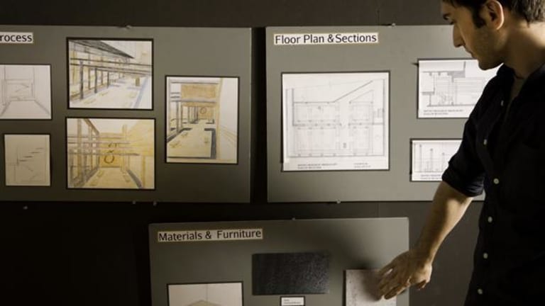 A man looking at a posters labled "Materials and Furniture" "Floor Plan & Sections" and a third one