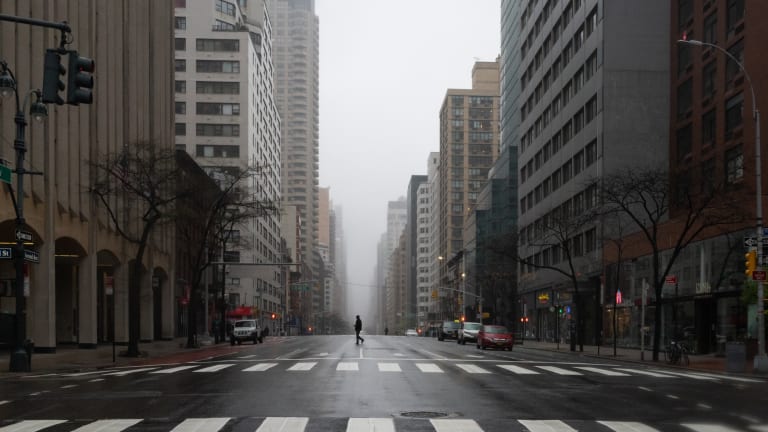 A Manhattan corridor is almost empty on a foggy, rainy day, as one person walks across the avenue. 