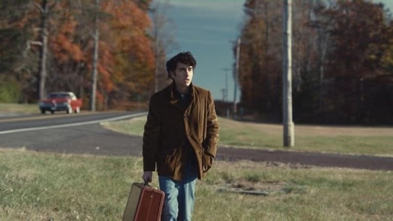 A man carrying a suitcase walking on grass towards something.