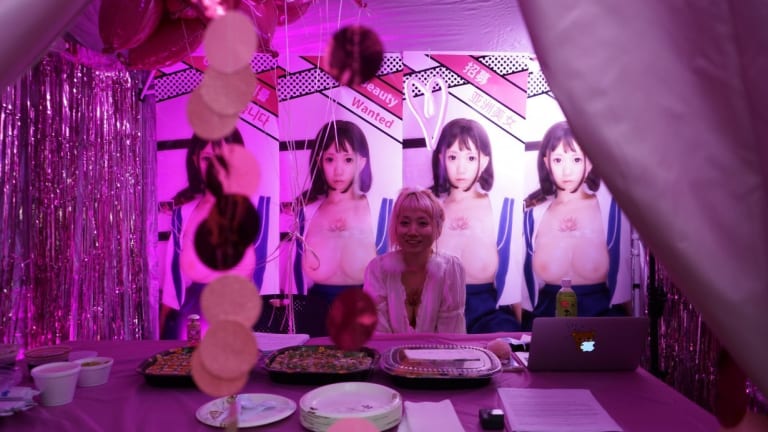 a person sits at a table surrounded by her artwork