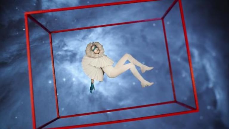 A costumed woman floating in a cube in space