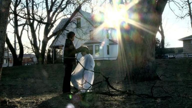 A woman gives someone a haircut outside in their backyard.