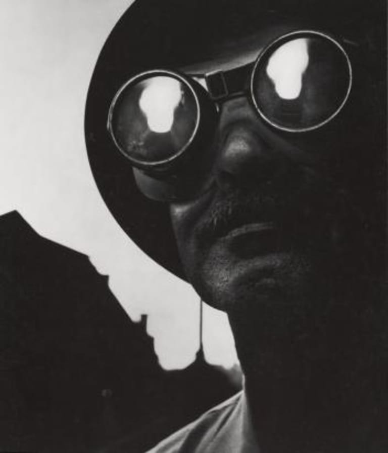 A black and white photo of a man with sun glasses and a hat.