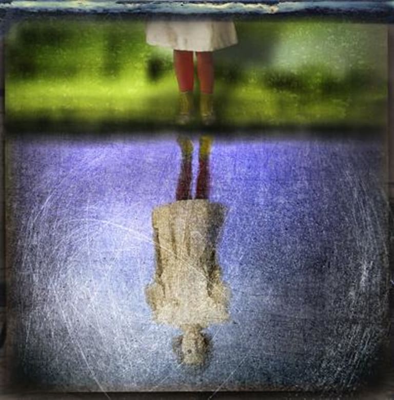 An alternative process photo shows the reflection of a young girl with red stockings.