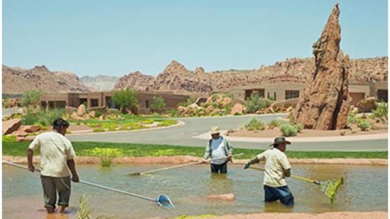 Three men are cleaning a small pond with nets and rakes.  They appear to be in the desert.