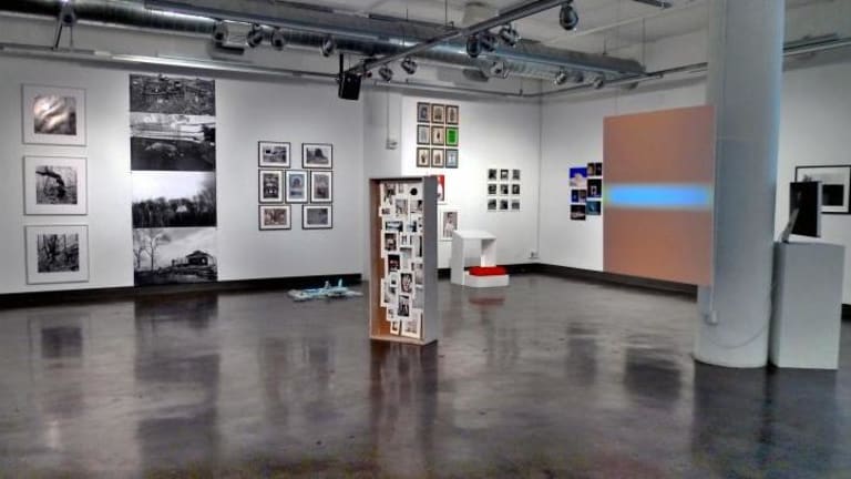 An art gallery featuring photographs in a variety of sizes on the walls and on a center display. It has exposed track lighting.