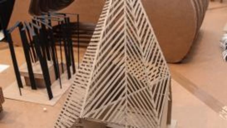 A model made of cardboard strips sits in front of a larger cardboard model.