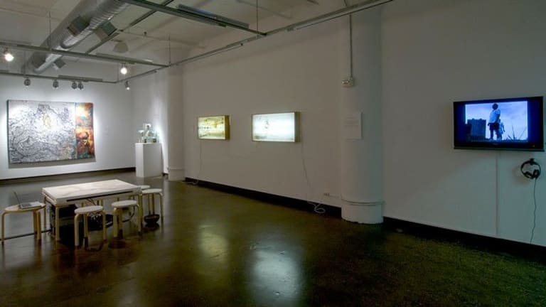 A large white room with a dining table on the floor, a TV on one wall and art work on the others.